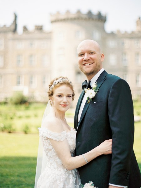 bride and groom stand in garden to wedding venue smiling