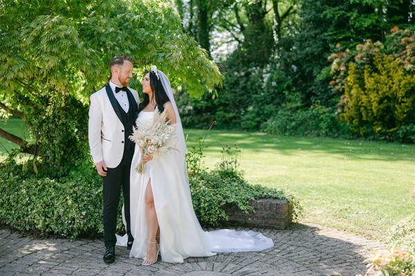 Bride and groom stand on pathway to garden park