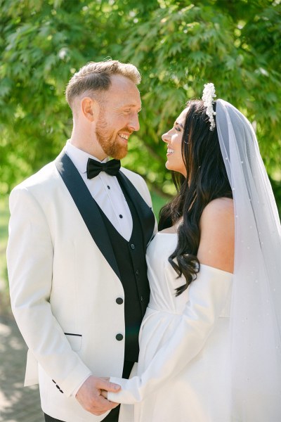 Bride and groom stand on pathway to garden park looking at each other