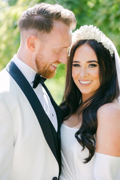 Bride and groom stand in park garden together and look at each other