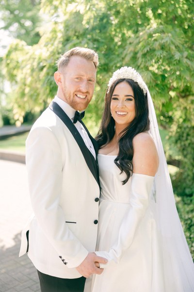 Bride and groom stand in park garden together and look at each other