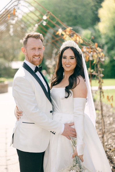 Bride and groom stand in park garden together and look at each other