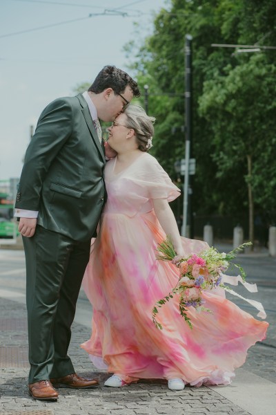 groom plants a kiss on brides forehead outside on street