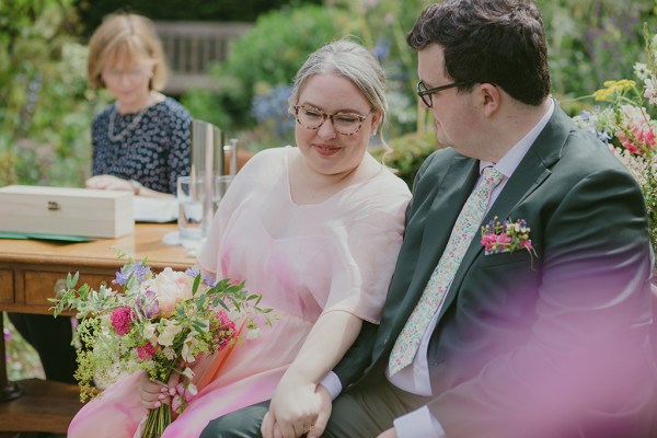 bride and groom sit holding hands during ceremony