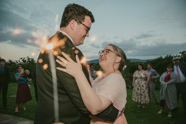 bride and groom dance hand in hand fireworks in background