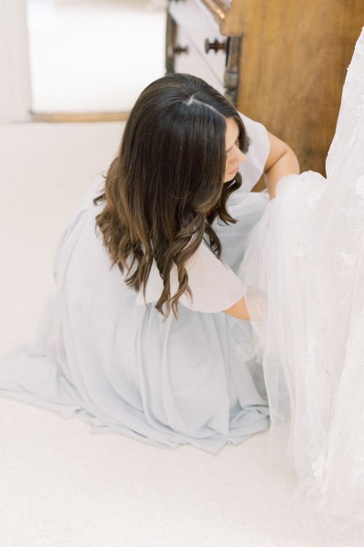 bridesmaid helps bride with gown dress