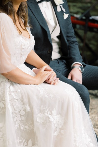 bride and groom hold hands as they are seated at alter