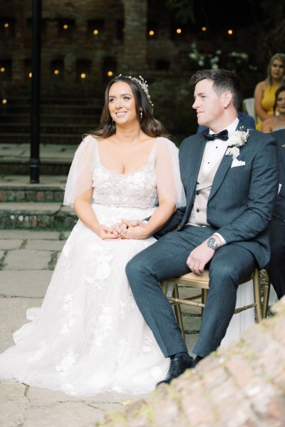 bride and groom hold hands as they are seated at alter they smile