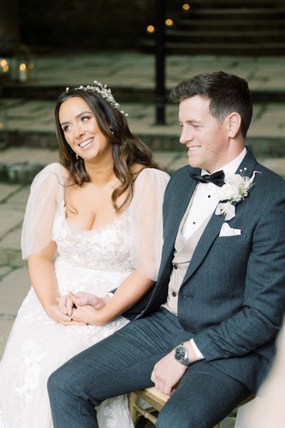 bride and groom hold hands as they are seated at alter