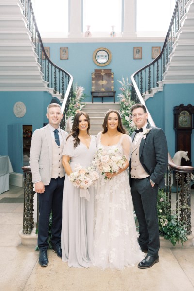 bride groom bridesmaid and father stand at the bottom of staircase