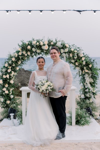 bride and groom pose in front of alter setting flower bed