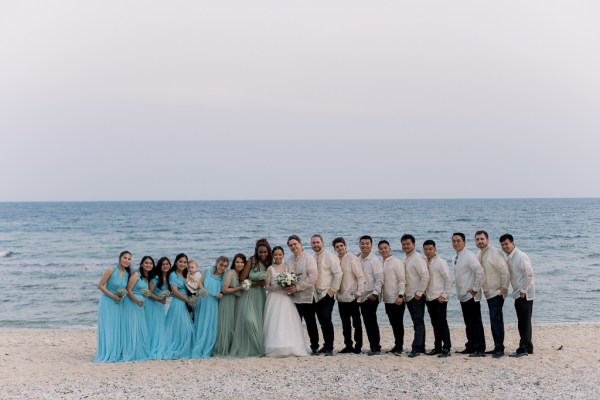 groom bride groomsmen bridesmaids holding flowers on the sandy beach