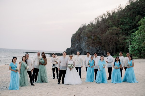 groom bride groomsmen bridesmaids holding flowers on the sandy beach