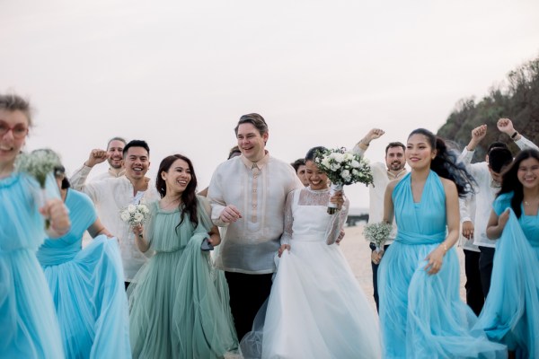 groom and bride in the middle of bridesmaids on the sand