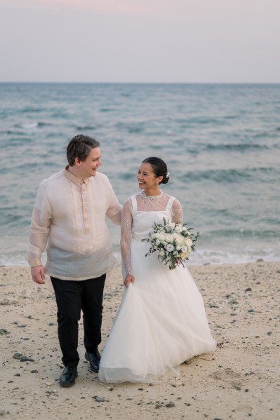 bride and groom walk on the sandy beach together