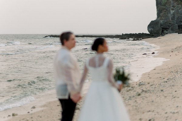 bride and groom walk on the sandy beach together