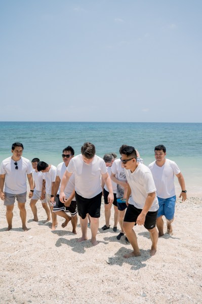 groom and his groomsmen playful on the sandy beach ocean sea in background