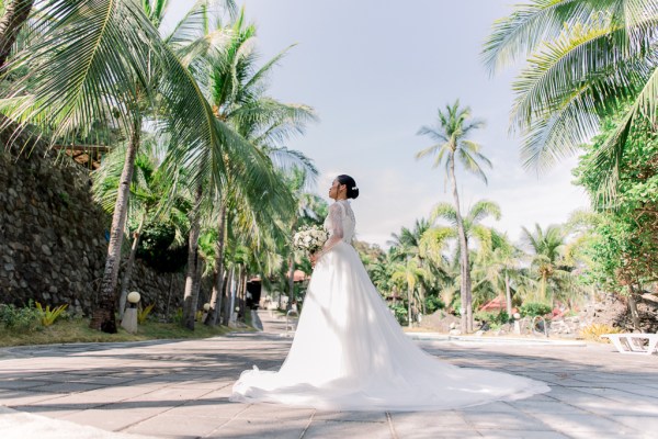 bride stands looking away from camera on the sand