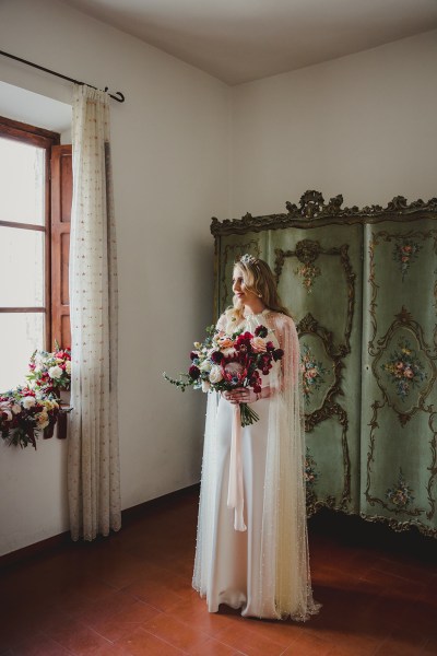 bride stands ready holding bouquet in room