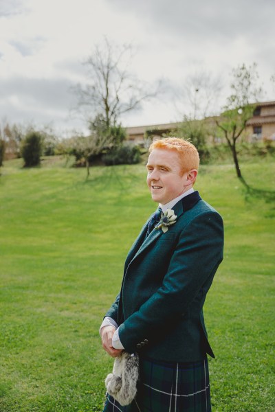 groom stands smiling on green grass at alter