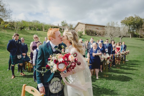 groom kisses bride on the cheek guests seated behind