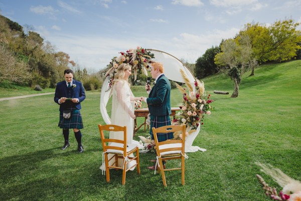 bride and groom in front of circular flower bed at alter to wedding they hold hands