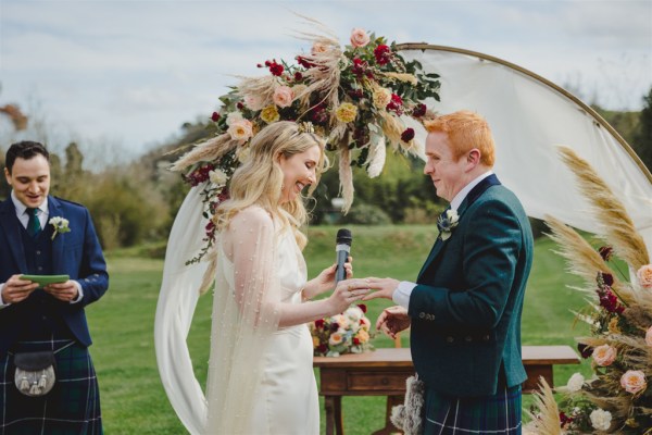 bride and groom in front of circular flower bed at alter to wedding they exchange wedding bands rings