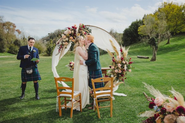 bride and groom in front of circular flower bed at alter to wedding they kiss