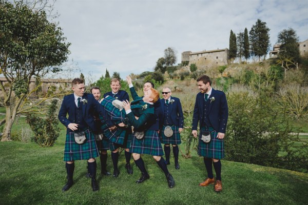 groom and his groomsmen mess around joking on the grass together