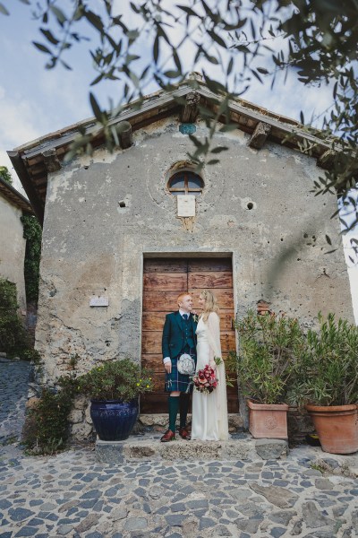 bride and groom pose in front of old abandoned house warehouse