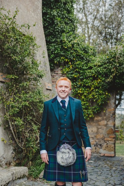 groom wearing kilt stands outside in garden