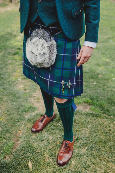 groom wearing kilt stands on the grass in garden