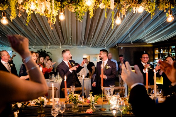 grooms smile cheer at the dining room table decor candles lit and guests surround