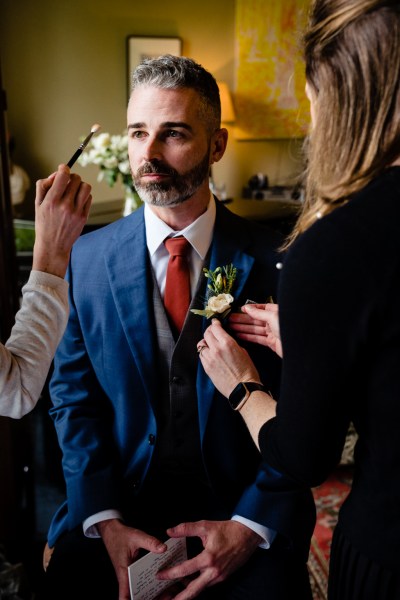 groom in blue suit helps with getting ready by female friend