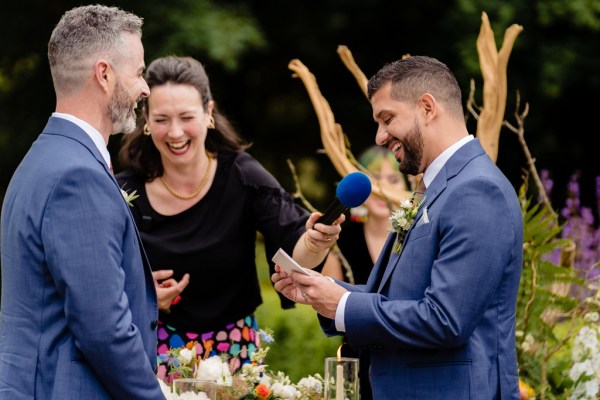 grooms laugh at alter during ceremony with celebrant holding microphone giving vows