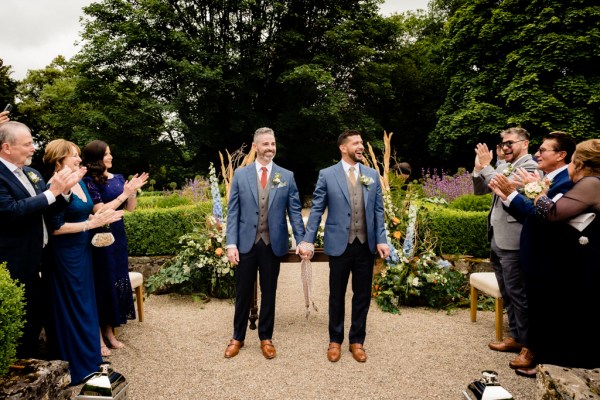 grooms stand in front of guests clapping for them