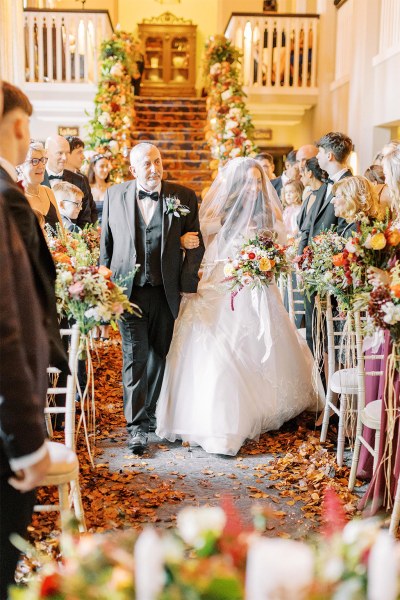 Father of the bride walks his daughter down the aisle she covers her face with veil guests watch