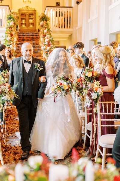 Father of the bride walks his daughter down the aisle she covers her face with veil guests watch