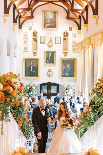 Bride and groom reach top of stairs with pumpkins flowers