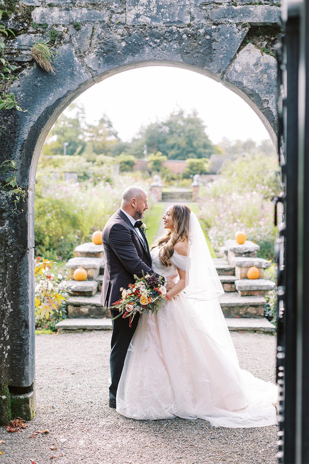 Bride and groom in garden under archway they face each other