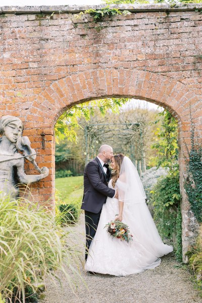 Bride holds bouquet as she stands with her groom under garden archway