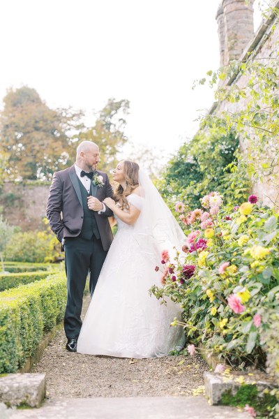 Bride and groom stop on pathway to garden and look at each other