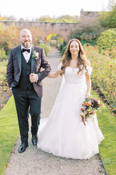 Bride and groom walk in the garden together linking arms