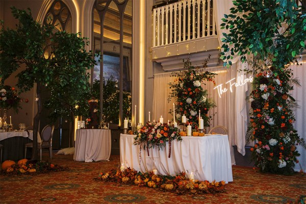 Balcony pumpkins on ground beside table covered in flowers and lit candles