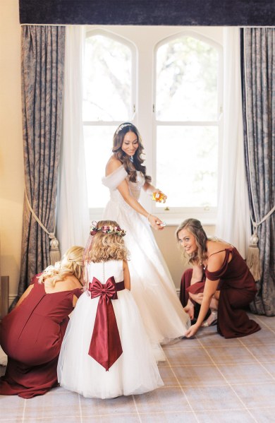 Bridesmaids help bride get ready beside large window