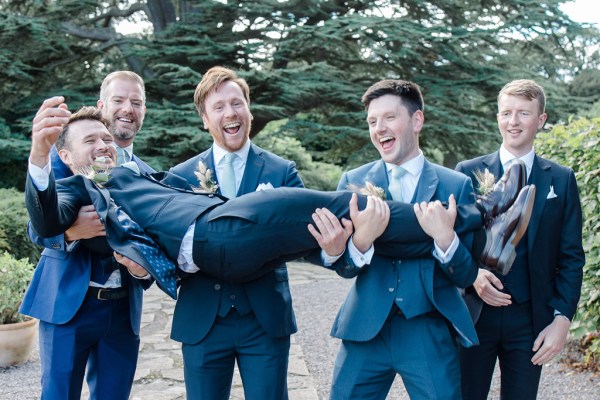 groomsmen hold up groom in garden