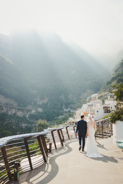 Groom and bride walk down path with mountains in the distance