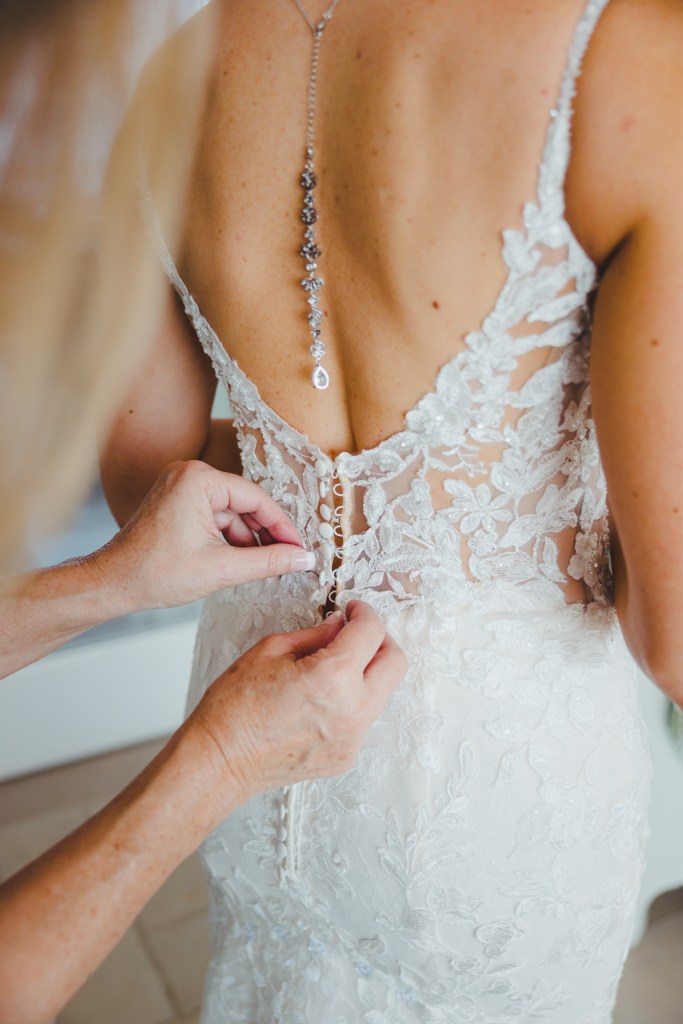 Mother of the bride buttoning up buttons on bride's lace dress