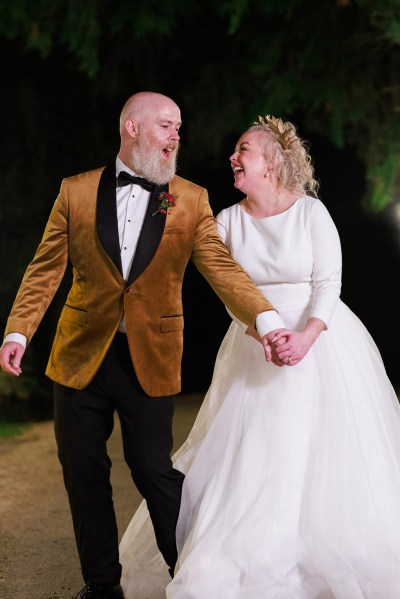 nighttime shot of bride and groom holding hands on the pathway laughing smiling