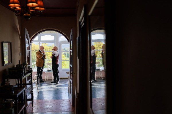 groom and groomsman are getting ready beside window